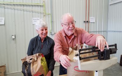 Two smiling volunteers weighing bagged seed