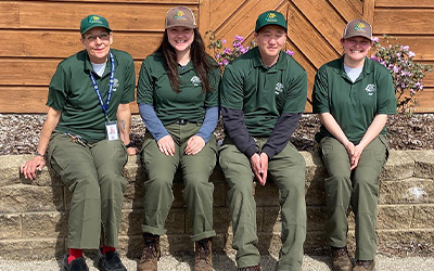 Four people sitting on a stone wall wearing ranger cadet uniforms